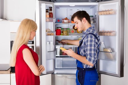 Young Woman Looking At Male Technician Checking Fridge With Digital Multimeter